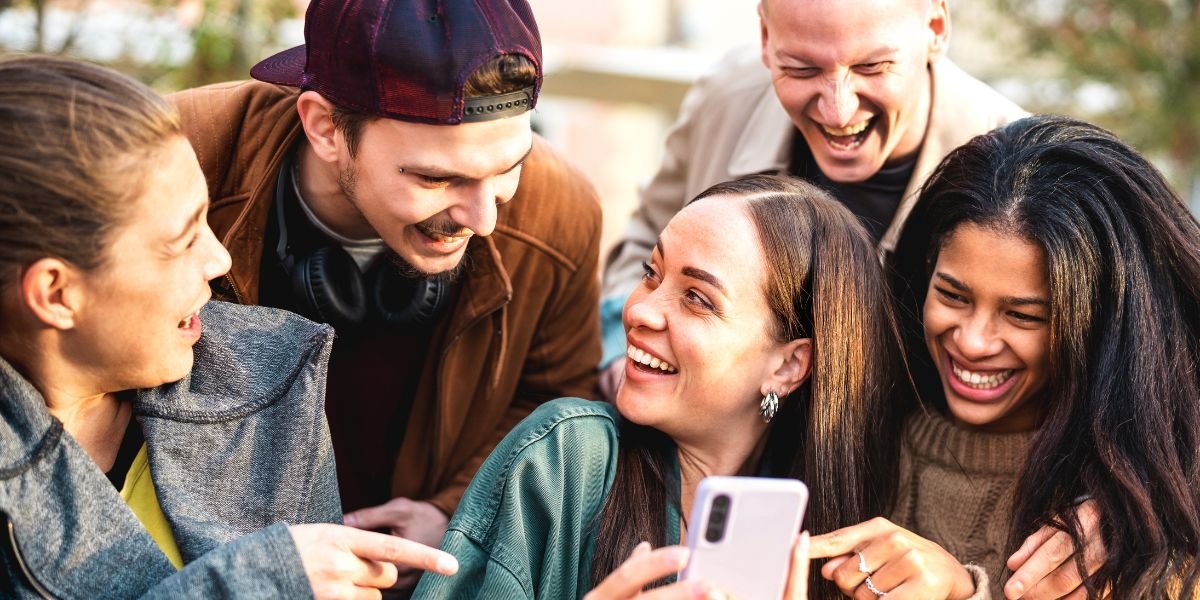 Group of colleagues laughing and pointing at a smartphone during a fun, affordable team outing
