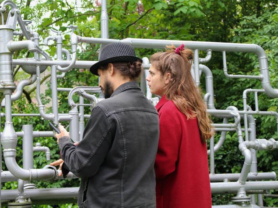 Twee leerlingen onderzoeken een metalen kunstwerk terwijl ze hun telefoon gebruiken tijdens het stadsspel City Detective van Qugato.